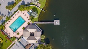 Vista aérea de un complejo turístico con piscina, un muelle que se adentra en un lago y un edificio con un techo octogonal distintivo.