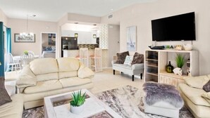 Amplia sala de estar con un sofá, una mesa de centro con una planta, un televisor y una cocina al fondo.