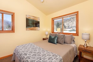Une chambre à coucher avec un lit, deux tables de chevet, une fenêtre donnant sur un paysage enneigé et un tableau accroché au mur.