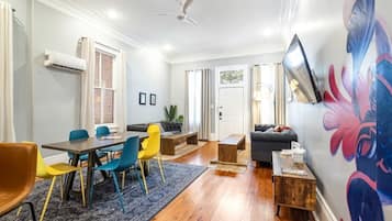 A modern living room with a dining area, a sofa, a coffee table, and a TV mounted on the wall.