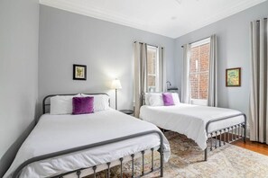 Une chambre avec deux lits, une fenêtre avec des rideaux, une lampe et un tableau au mur.