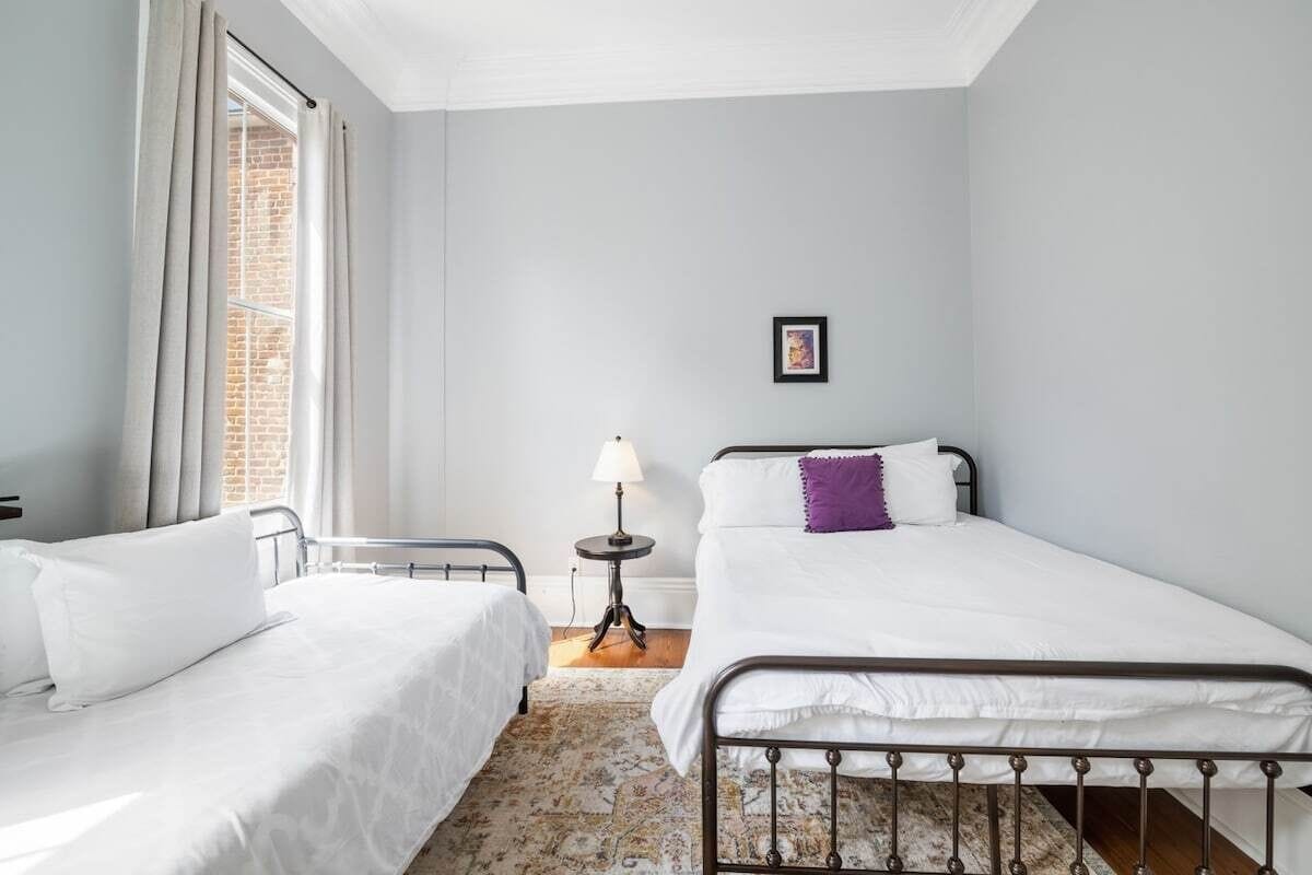A bedroom with two beds, a small table with a lamp, and a picture on the wall.