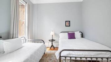 A bedroom with two beds, a small table with a lamp, and a picture on the wall.