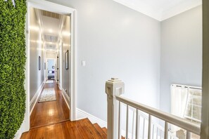Un pasillo con suelo de madera, paredes blancas y una pared verde en un lateral.