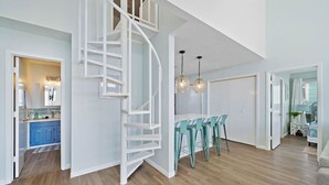 A modern interior with a spiral staircase, a kitchen with blue cabinets, a dining area with teal chairs, and pendant lighting.