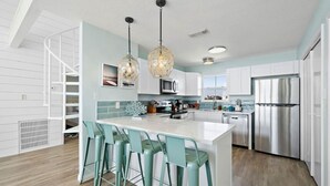 A modern kitchen with a central island, bar stools, stainless steel appliances, and pendant lighting.