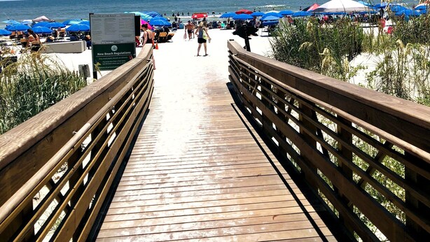 A wooden boardwalk leading to a beach with blue umbrellas and a sign indicating new beach regulations. - HUGE 4 BR/3 BATH Villa 15 minute walk to Beach (3 min walk to the pool) (Hilton Head Island)