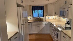 A compact kitchen with white cabinets, a wooden floor, a microwave, a kettle, and a window with a view of a fence. - HUGE 4 BR/3 BATH Villa 15 minute walk to Beach (3 min walk to the pool) (Hilton Head Island)