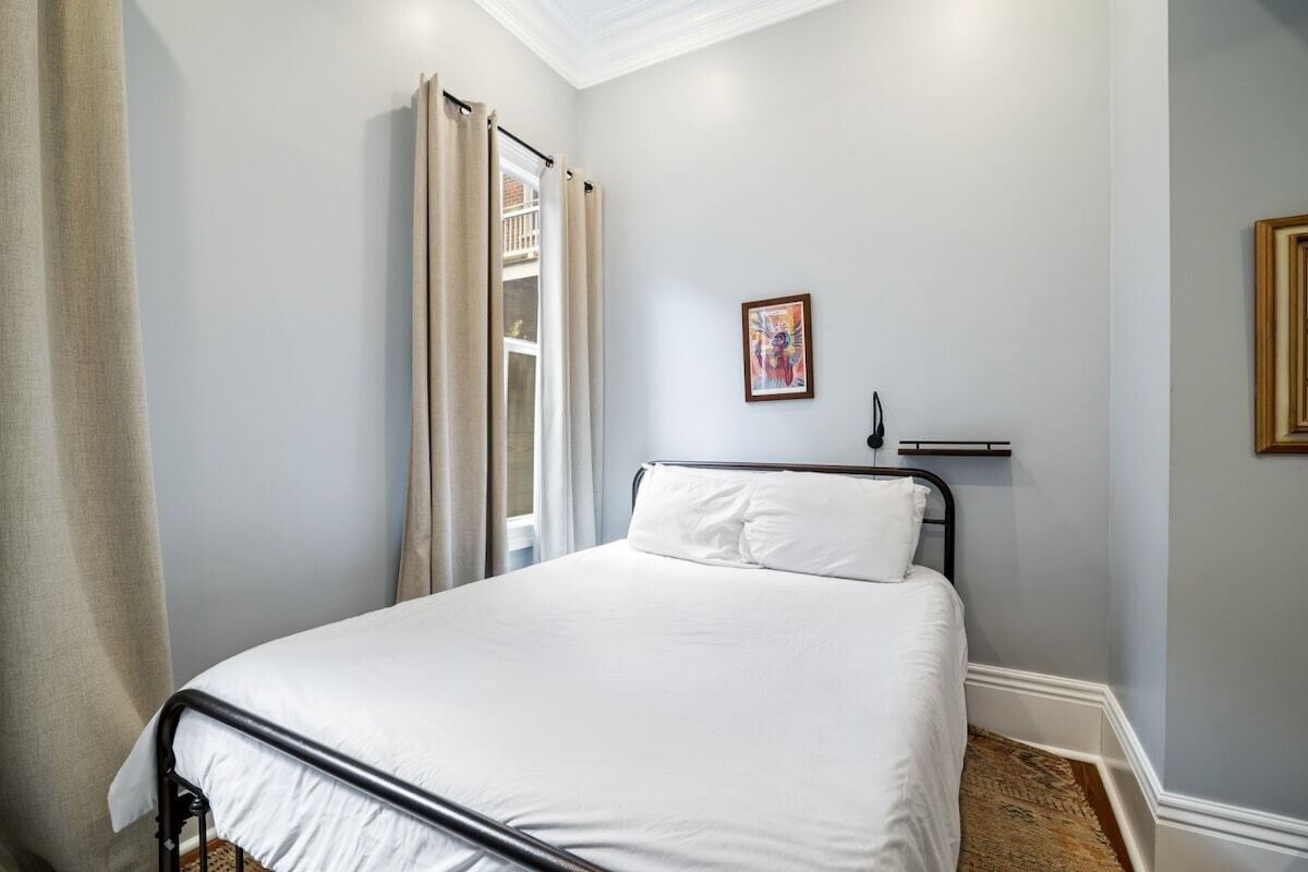 Een slaapkamer met een bed, een raam met gordijnen, een schilderij aan de muur en een houten vloer.