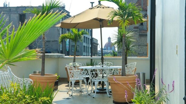 A rooftop terrace with white wrought iron furniture, terracotta planters, and a beige umbrella. - Hotel Habana (Mexico City)