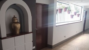 A hallway with a tiled floor, a white reception desk with a gold vase, and a window with potted plants. - Hotel Habana (Mexico City)