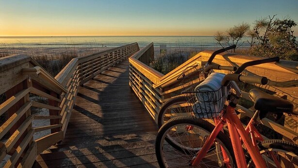 Une promenade en bois menant à une plage, avec un vélo garé dessus.