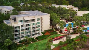 Un hôtel à plusieurs étages doté d’une piscine, entouré d’une végétation luxuriante et situé près d’une plage.
