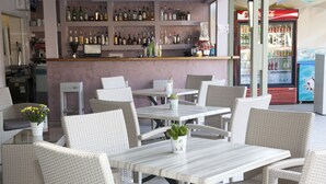 Een bar met rieten meubels en diverse drankflessen op planken.