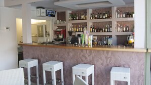 Een bar met een toog, flessenplanken en witte rieten stoelen.