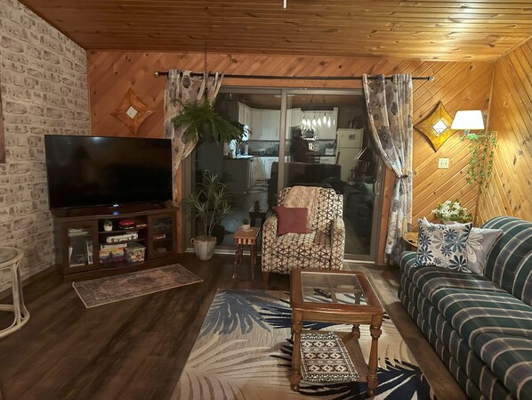 Un salon confortable avec un téléviseur, un canapé et un coin repas visible à travers une porte vitrée.