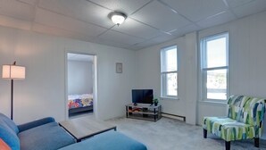 A living room with a blue sofa, a colorful armchair, a TV on a wooden stand, and a lamp. - Parkview, Apt #5
Parkview Historic Apartment (Hershey)