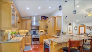 Una cocina con armarios de madera, una campana extractora de acero inoxidable, un horno empotrado y una zona de bar con taburetes.
