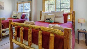 Un dormitorio con dos camas, cabeceros de madera, una ventana y una mesita de noche con lámpara.