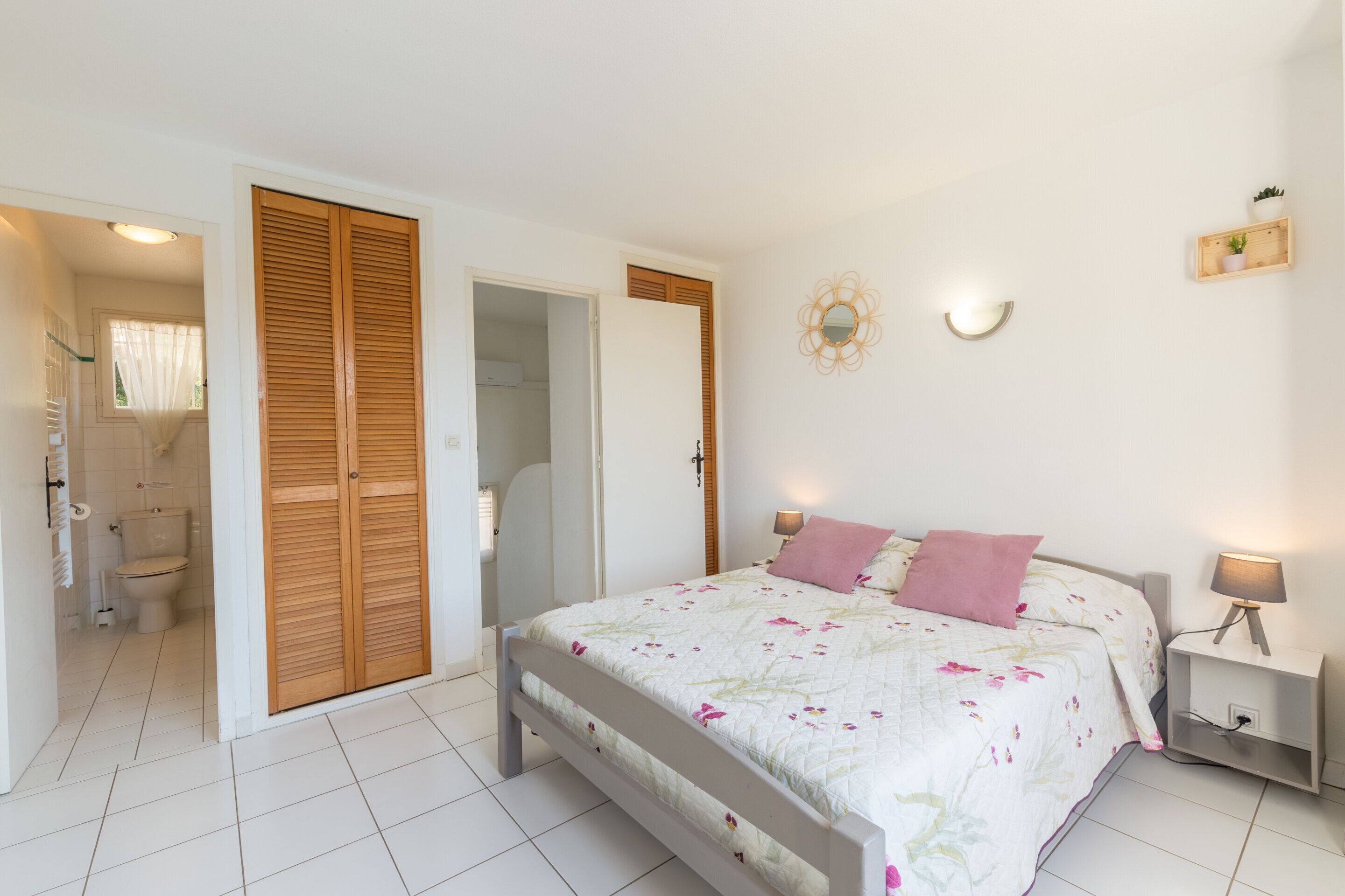 Quarto com cama, abajures, mesa de cabeceira, espelho e luminária na parede.