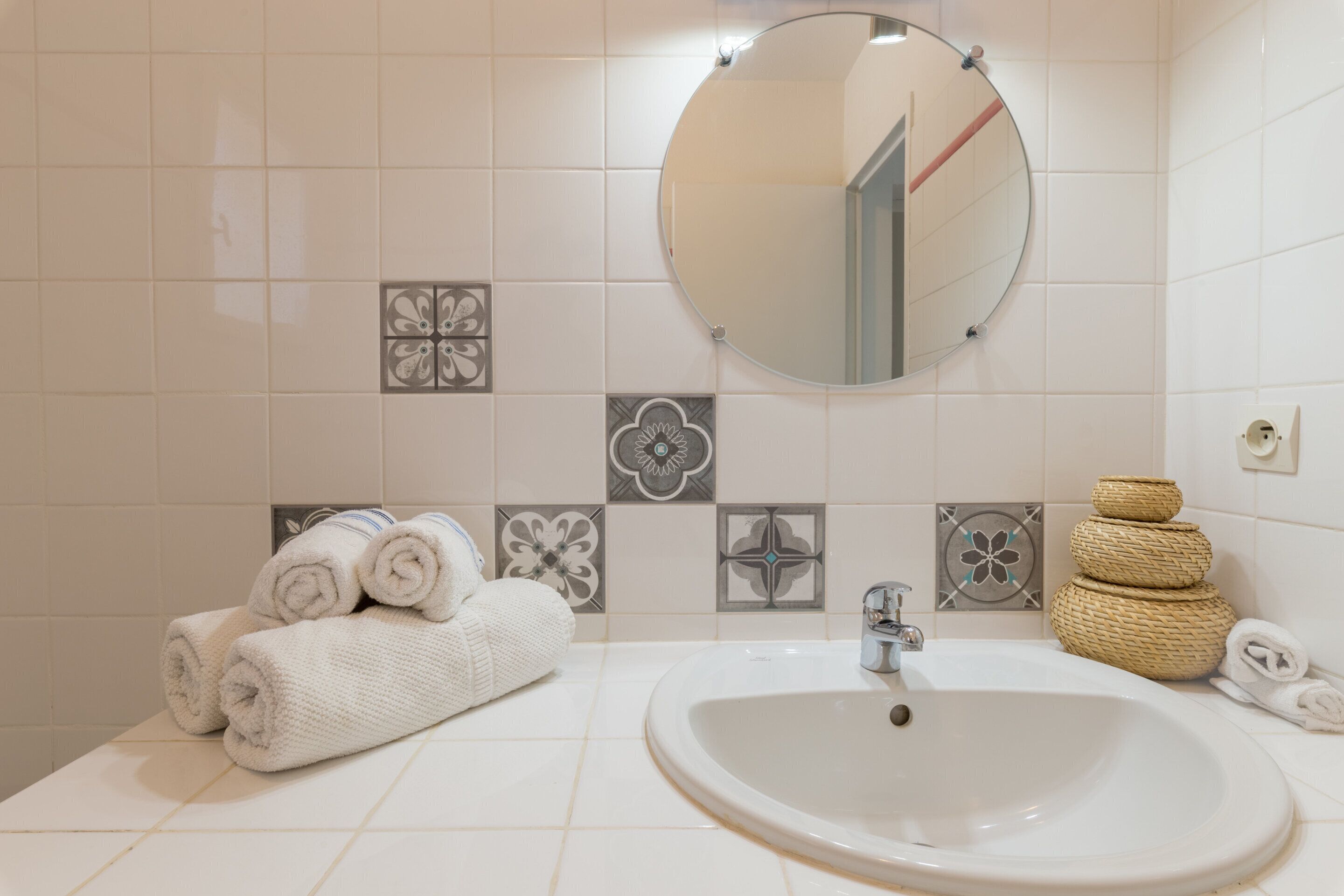 A bathroom with a sink, mirror, and decorative tiles.
