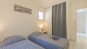 A bedroom with two beds, a nightstand, a lamp, a painting, and a door.