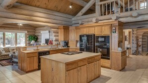 A spacious log cabin kitchen with wooden cabinetry, a large island, and a dining area with a view of the outdoors. - Eagle's Landing- Beach Front Log Home  - RARE FIND on Beautiful Woman Lake! (Longville)