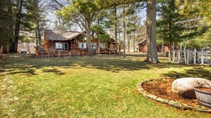 A rustic cabin with a deck, surrounded by trees. - Eagle's Landing- Beach Front Log Home  - RARE FIND on Beautiful Woman Lake! (Longville)