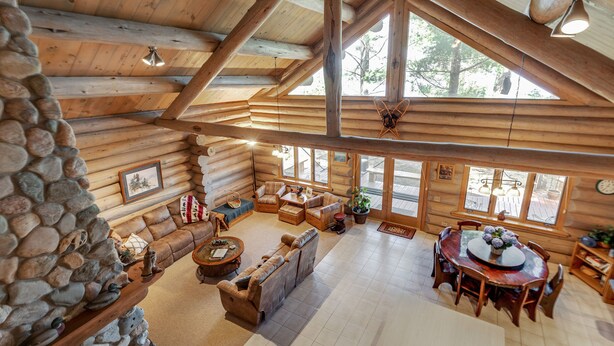 A log cabin interior with a stone fireplace, wooden furniture, and large windows. - Eagle's Landing- Beach Front Log Home  - RARE FIND on Beautiful Woman Lake! (Longville)
