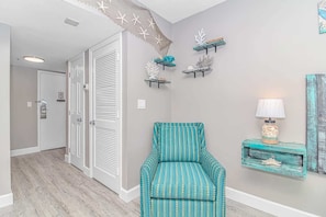 A hallway with a teal patterned chair, a wall-mounted lamp, and decorative coral pieces.