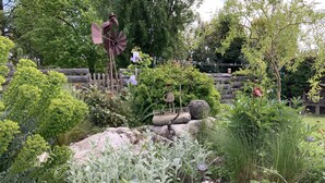Un jardí amb un molí de vent, plantes diverses i una tanca de fusta.