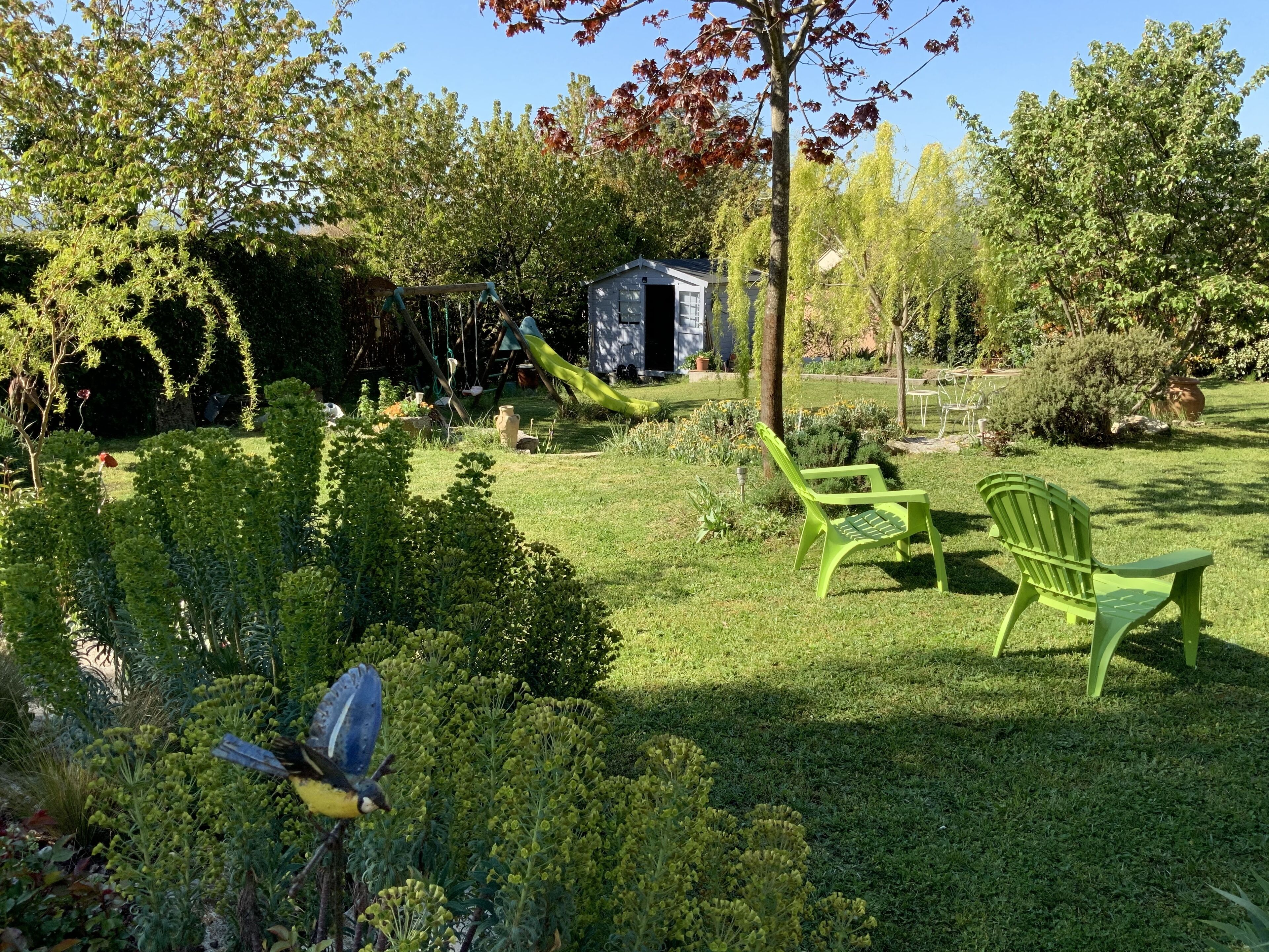 Ein gepflegter Garten mit Spielbereich, darunter Schaukel und Rutsche, umgeben von üppiger Vegetation und einem kleinen Gartenhaus.