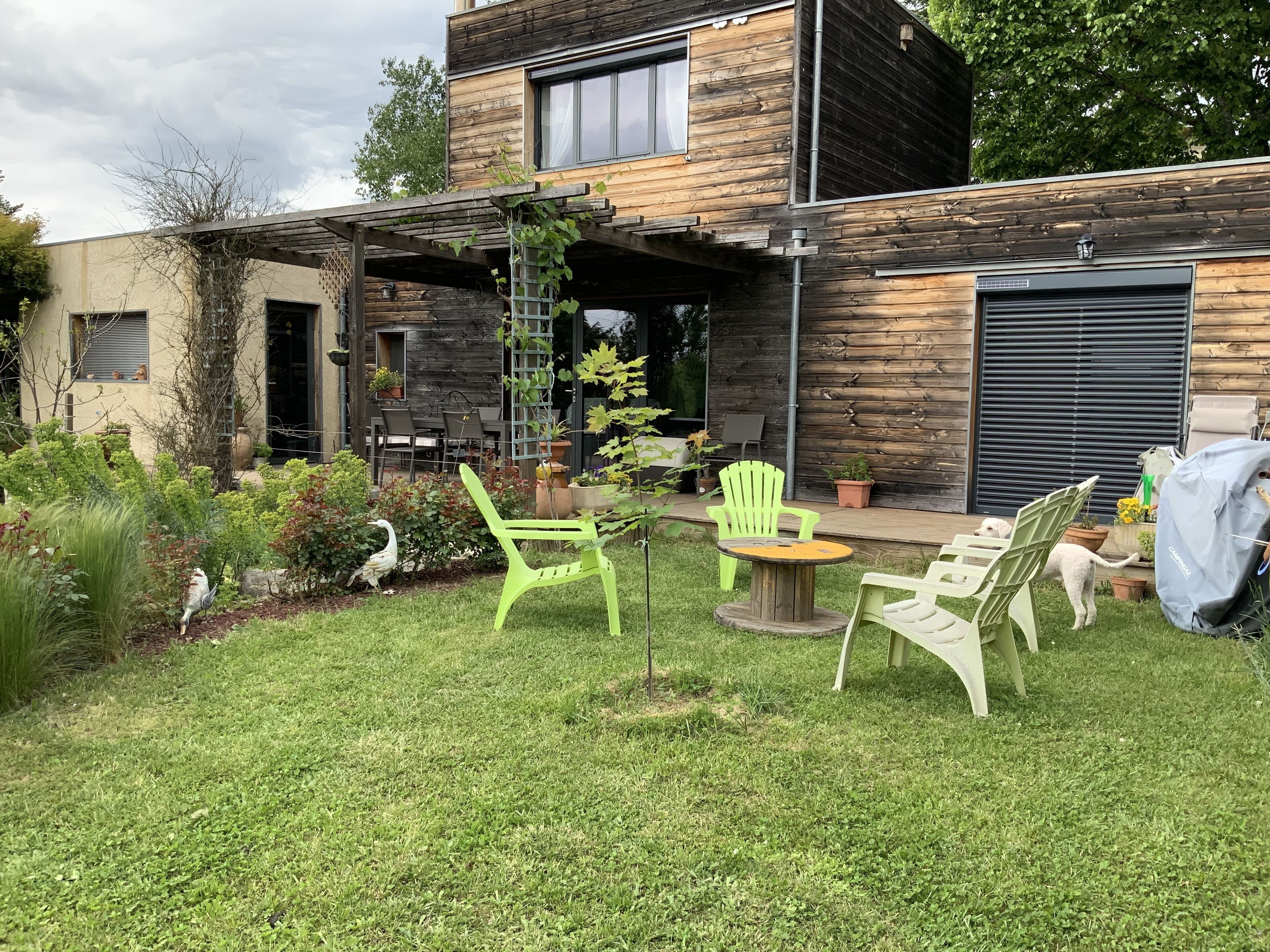 A modern house with a wooden exterior, a covered patio with outdoor furniture, and a well-maintained garden.