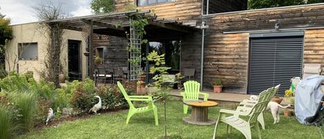 A modern house with a wooden exterior, a covered patio with outdoor furniture, and a well-maintained garden.