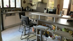 Una cuina moderna amb una illa central, tamboretes de bar i diversos electrodomèstics.