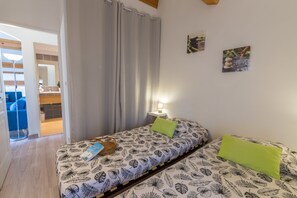 A bedroom with two beds, a nightstand, a lamp, and a view of a dining area.