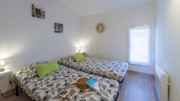 Ein Schlafzimmer mit zwei Betten, einem Fenster und einem Wandspiegel.