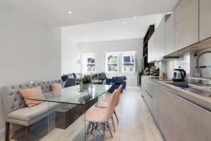 A modern kitchen with a glass dining table, grey sofas, and a view of the city. - Stunningly Decorated 3BD Flat in Fulham (London)