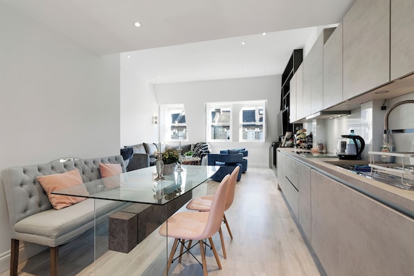 Una cocina moderna con una mesa de comedor de vidrio, sofás grises y vistas a la ciudad.