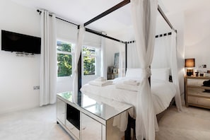 Un dormitorio moderno con una cama con dosel, una mesita de noche, un televisor de pantalla plana montado en la pared y un gran ventanal con cortinas.