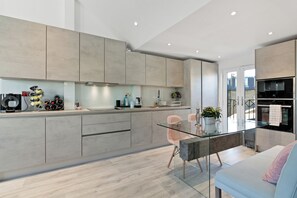 Une cuisine moderne avec une table à manger en verre, des meubles de rangement gris et un four encastré.