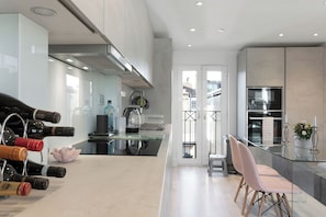 A modern kitchen with a glass dining table, stainless steel appliances, and wine bottles on the counter. - Stunningly Decorated 3BD Flat in Fulham (London)