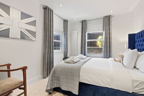 Ein zeitgemäßes Schlafzimmer mit einem Bett, einem Sessel und einem Fenster mit Vorhängen.