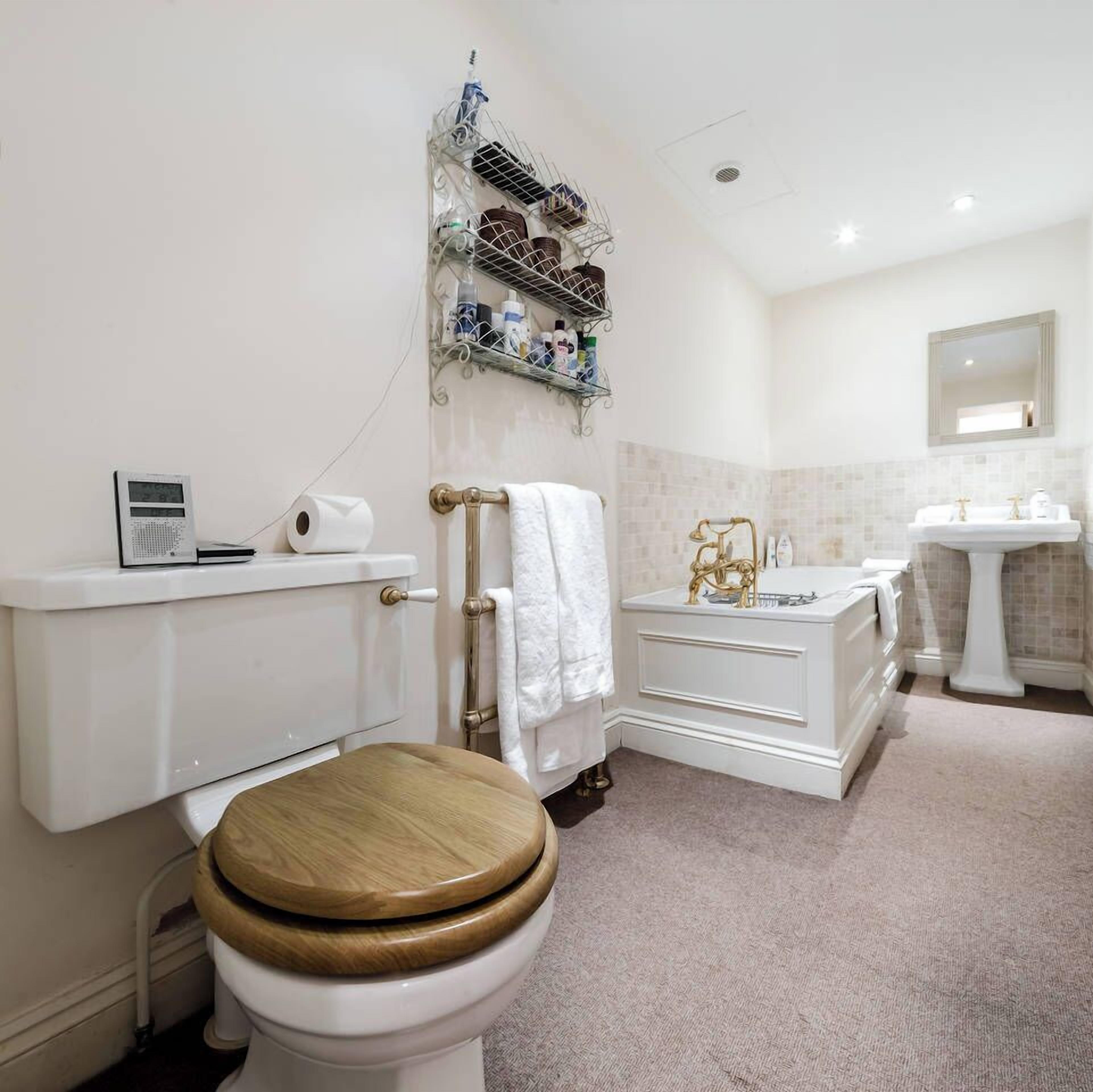 Een badkamer met toilet, wastafel en douche. Boven het toilet bevindt zich een plank met toiletartikelen.