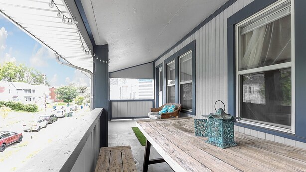 Een overdekte veranda met een houten bank, een rieten stoel en een decoratieve lantaarn.