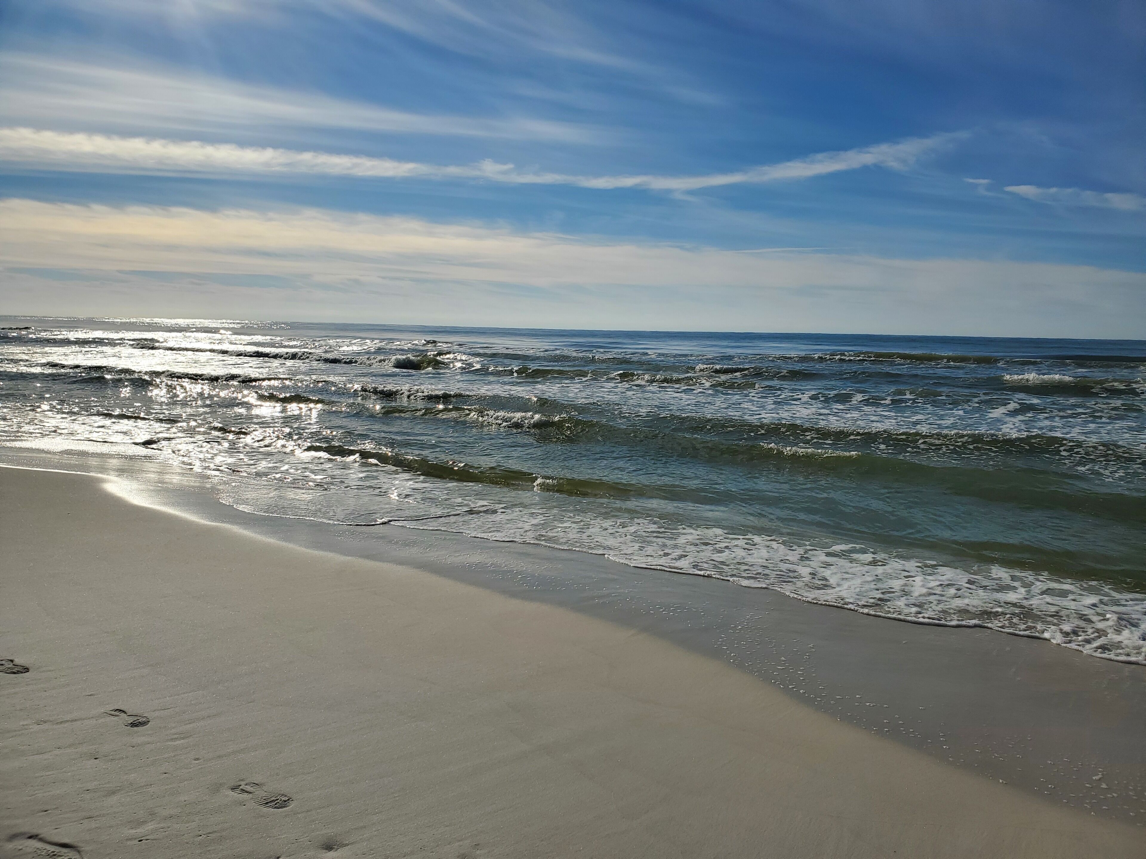 Ein Strand mit Wellen, blauem Himmel und Fußabdrücken im Sand.