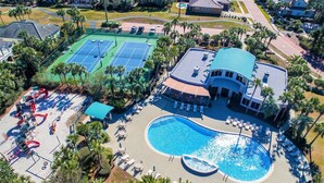 Vue aérienne d’un complexe hôtelier doté d’une grande piscine, de courts de tennis et d’un espace extérieur aménagé avec des sièges, protégé par un auvent.
