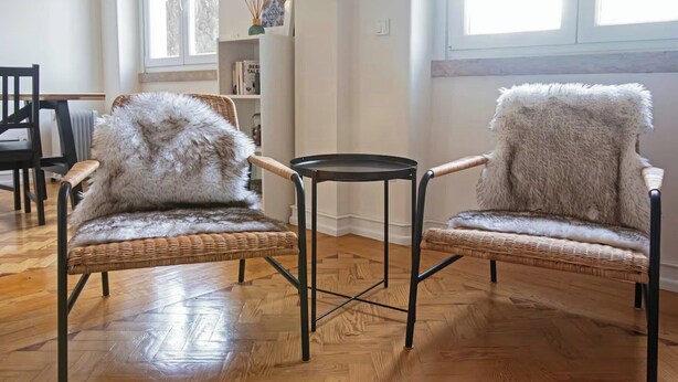 Two wicker chairs with fur throws, a small round table, and a bookshelf in a room with wooden flooring and large windows. - Cosy 1 BDR Apt Belem Sleeps 4 (Lisboa)