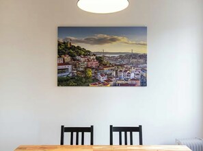 A dining area with a table and two chairs, a cityscape painting on the wall, and a radiator below.