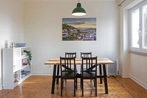 Ein Essbereich mit einem Holztisch und Stühlen, einer hängenden Pendelleuchte, einem Bücherregal und einem Stadtbild an der Wand.
